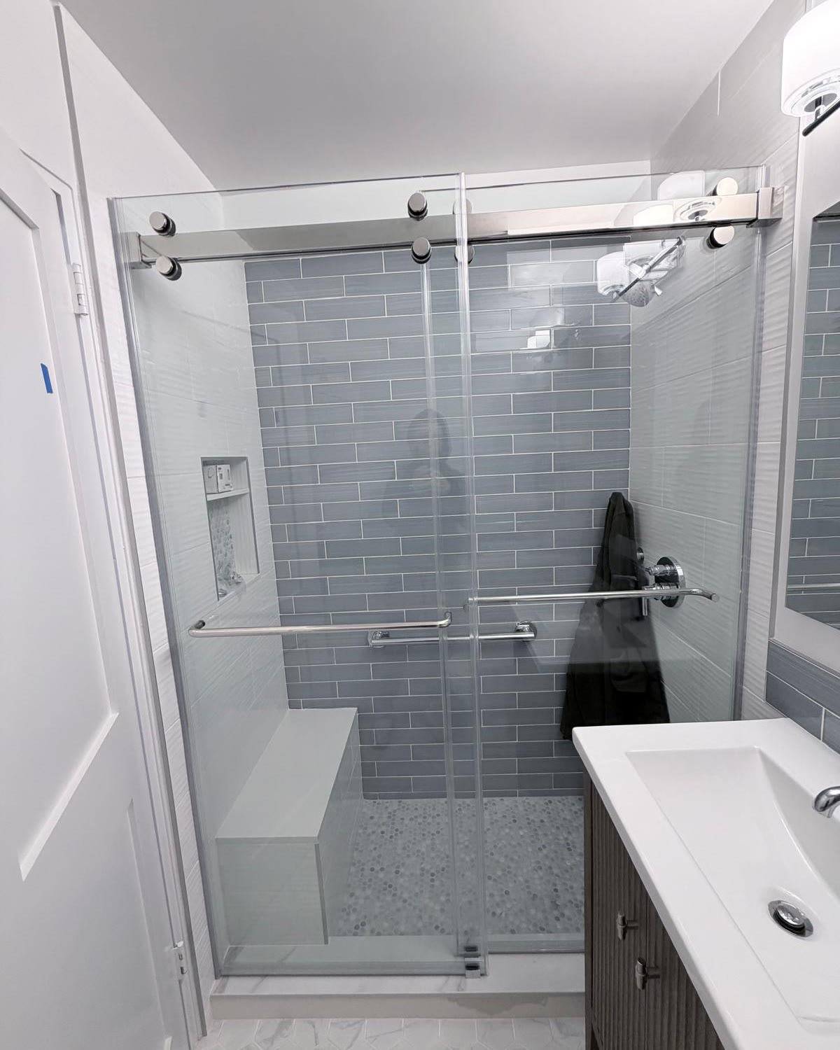 Finished sliding shower door at 84 Clinton, Lower East Side Manhattan, with chrome hardware and gray tile backdrop.