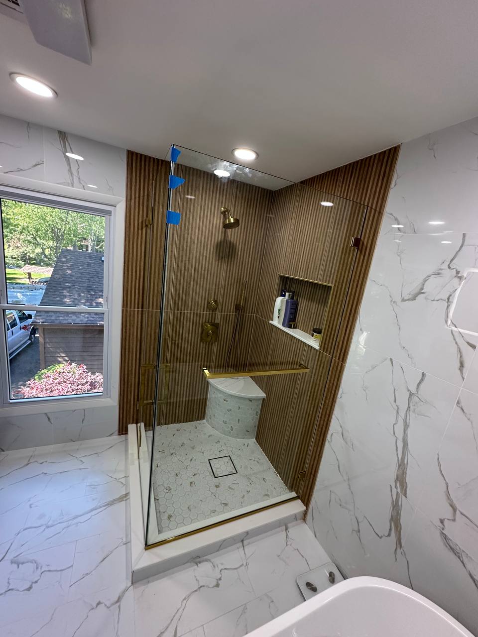 Clear tempered shower door in an Edison NJ bathroom with brushed brass hardware and warm tile finishes