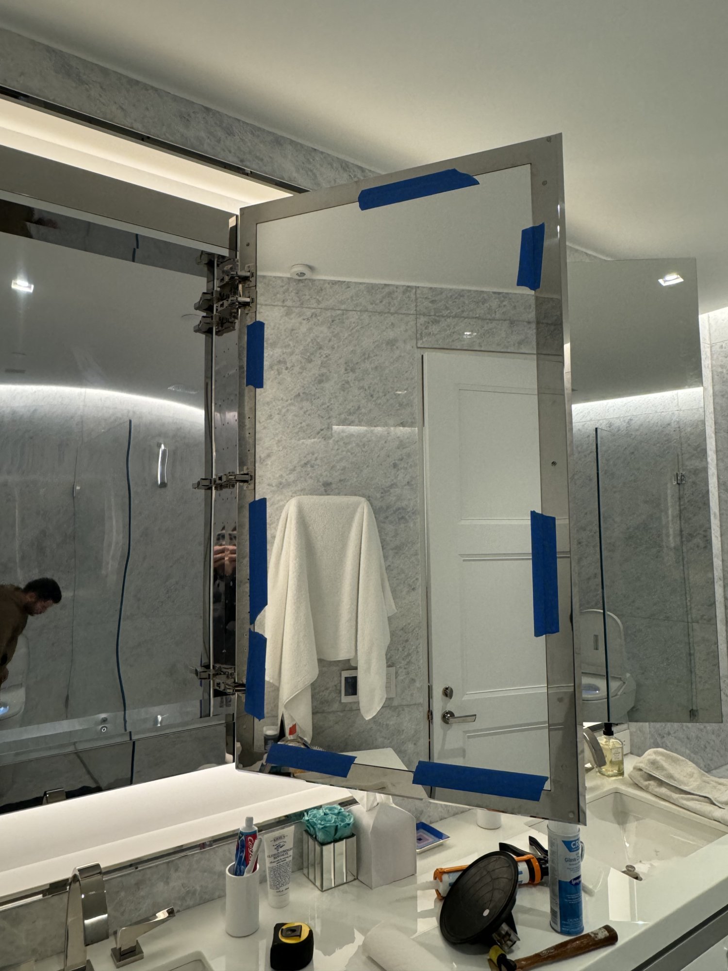 Medicine cabinet mirror with blue tape during silicone curing in NYC apartment