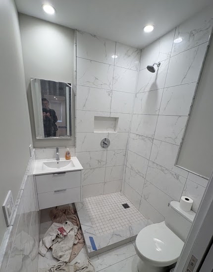 Open shower area before frameless glass installation, white marble tile throughout, floating vanity and built-in niche visible