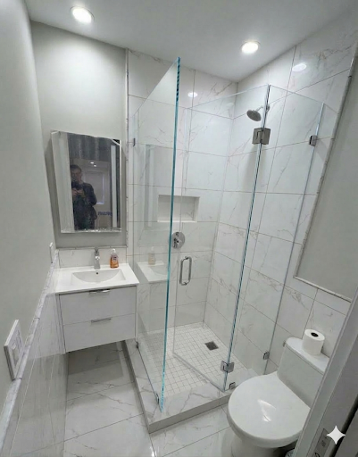 Hinged frameless shower enclosure with fixed panel and chrome hardware in white marble tile bathroom NYC
