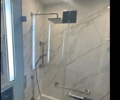 Tub enclosure detail with clear glass, rectangular chrome fittings, a horizontal handle and white veined wall tile.