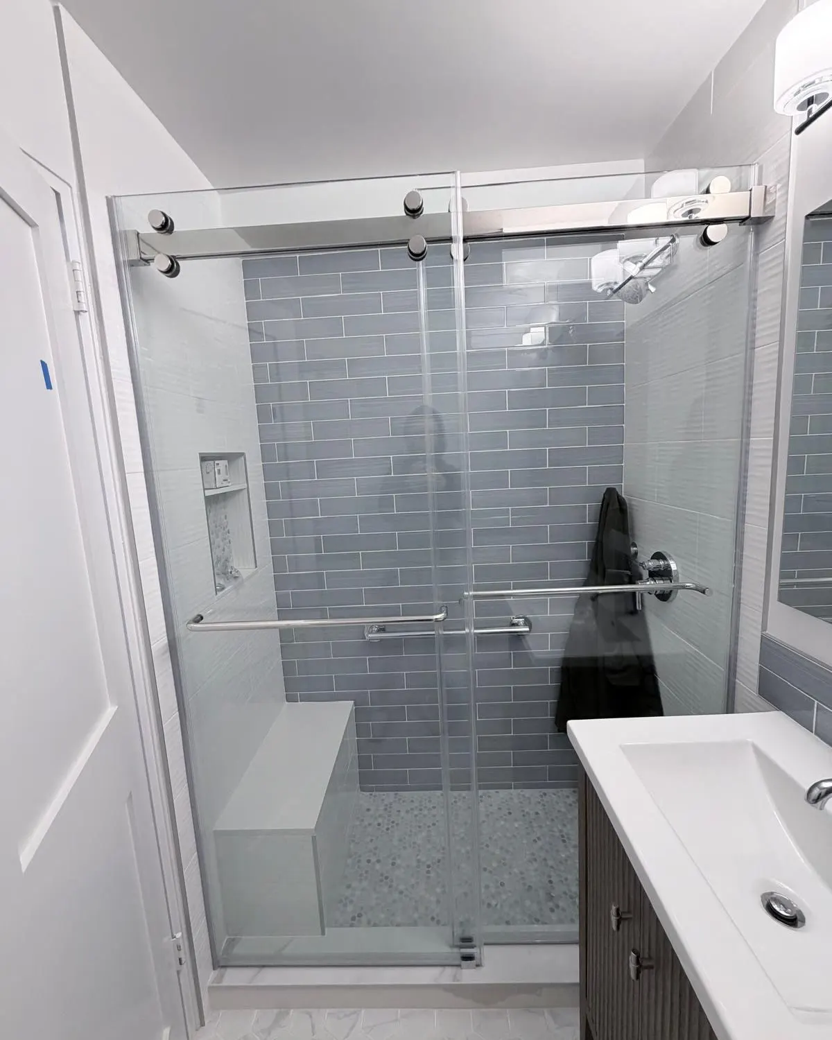 Finished sliding shower door at 84 Clinton, Lower East Side Manhattan, with chrome hardware and gray tile backdrop.